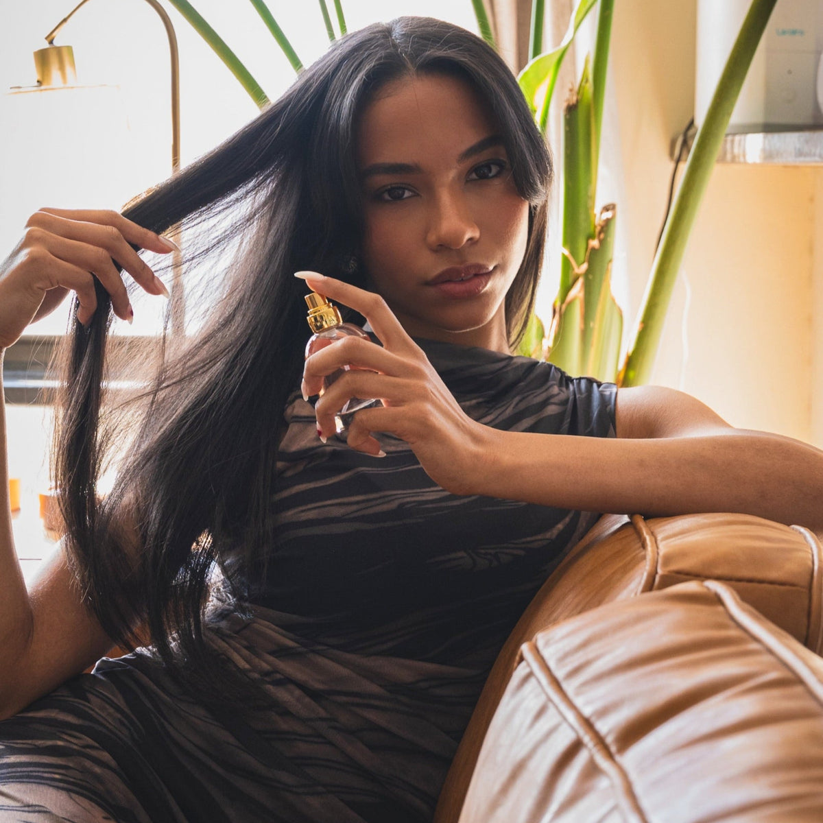 woman sitting on a couch holding up hair perfume to her hair